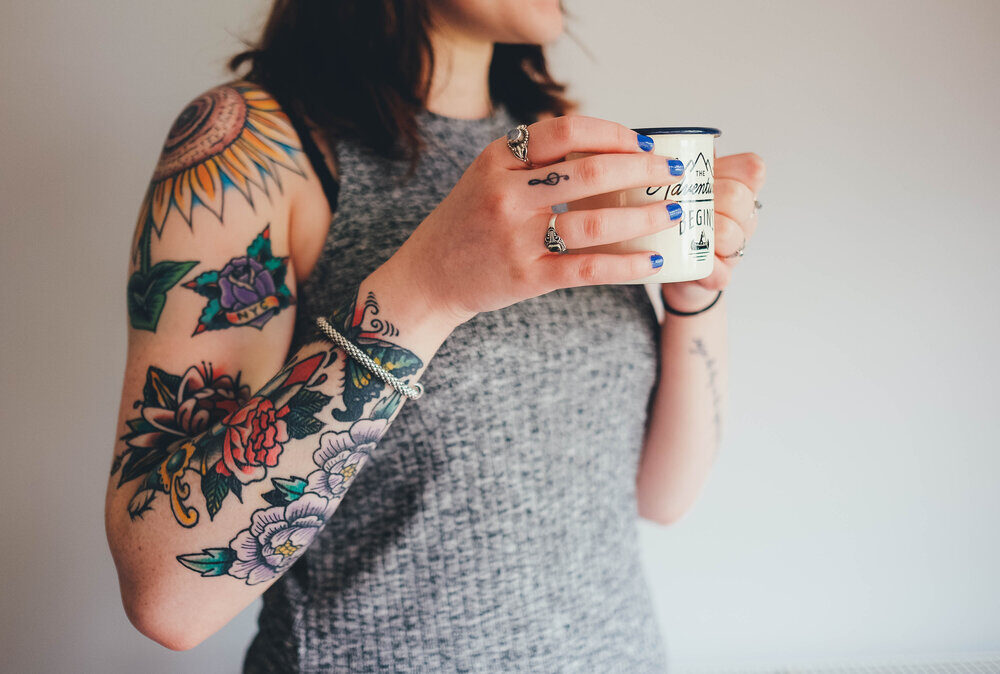 girl with arm tattoo drinking from a mug