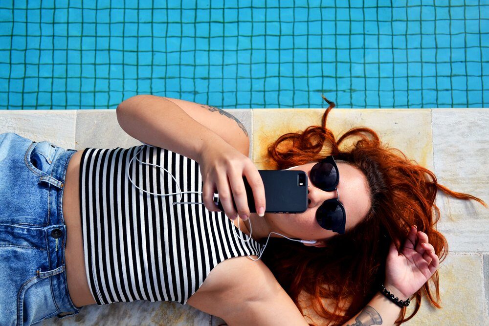 girl lying by the pool in sunglasses and black and white striped tank top