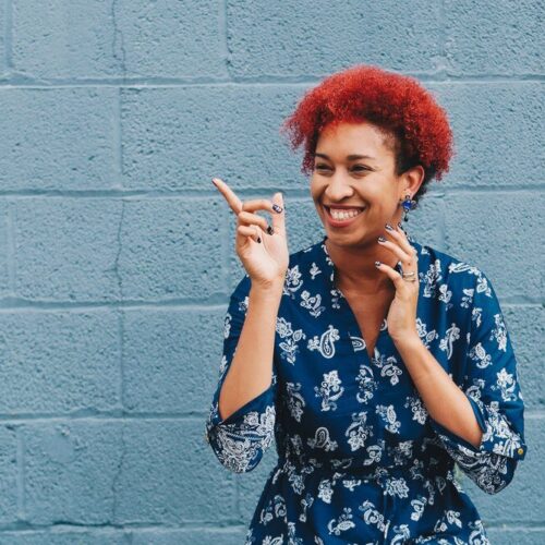 black woman with red hair pointing in front of a blue wall