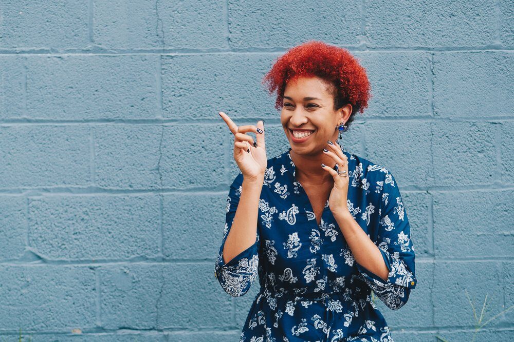 black woman with red hair pointing in front of a blue wall