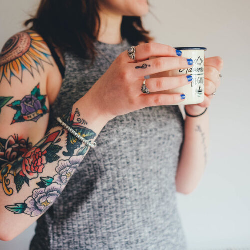 girl with arm tattoo drinking from mug