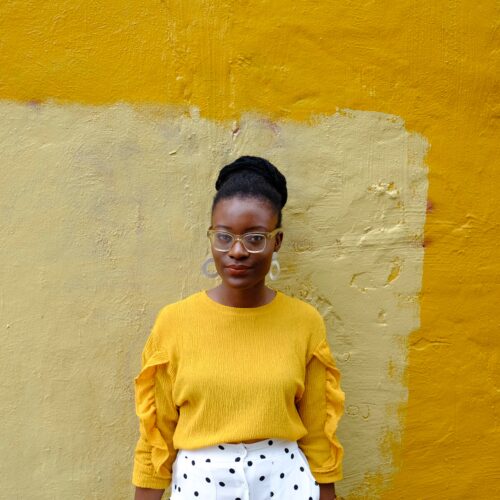 woman in yellow crew neck long sleeve shirt leaning on yellow painted wall